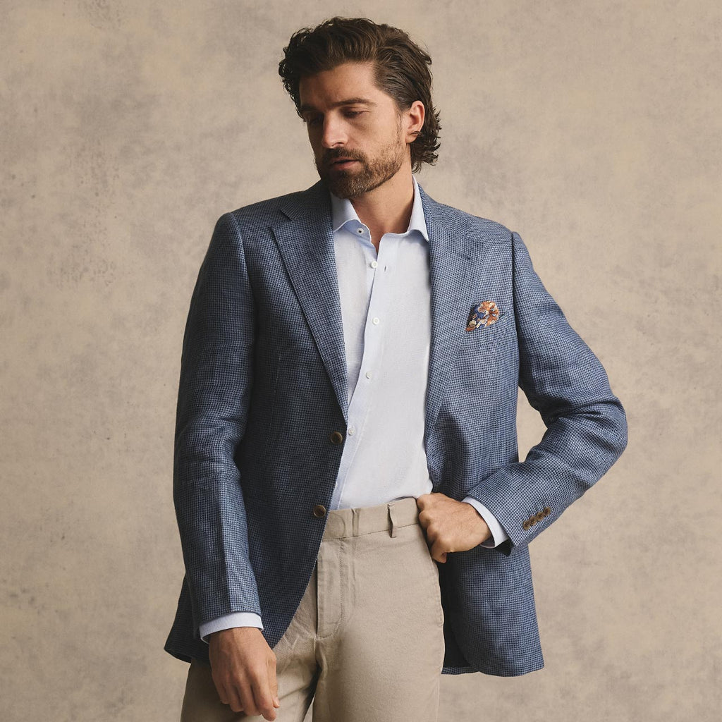 Man wearing a blue blazer over a white shirt with beige pants against a beige background