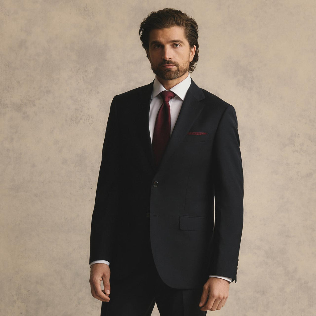 Man wearing a black suit with a red tie against a beige background