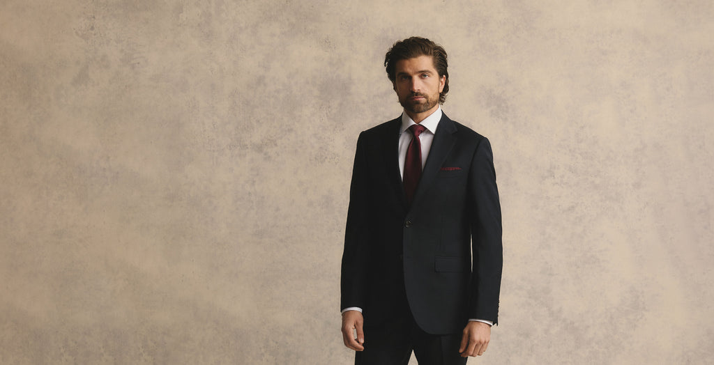Man wearing a dark suit with a red tie against a beige background