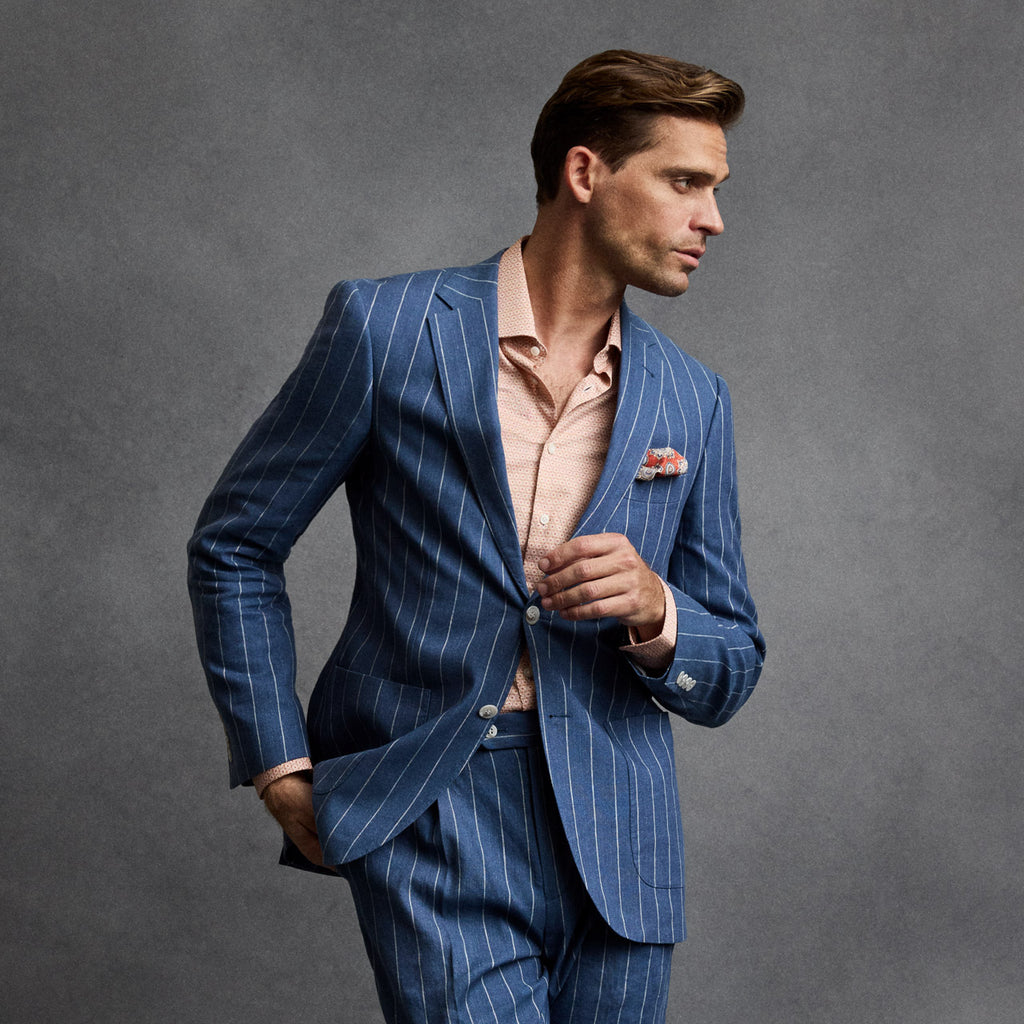 Man wearing a blue pinstripe suit with a pink shirt against a gray background