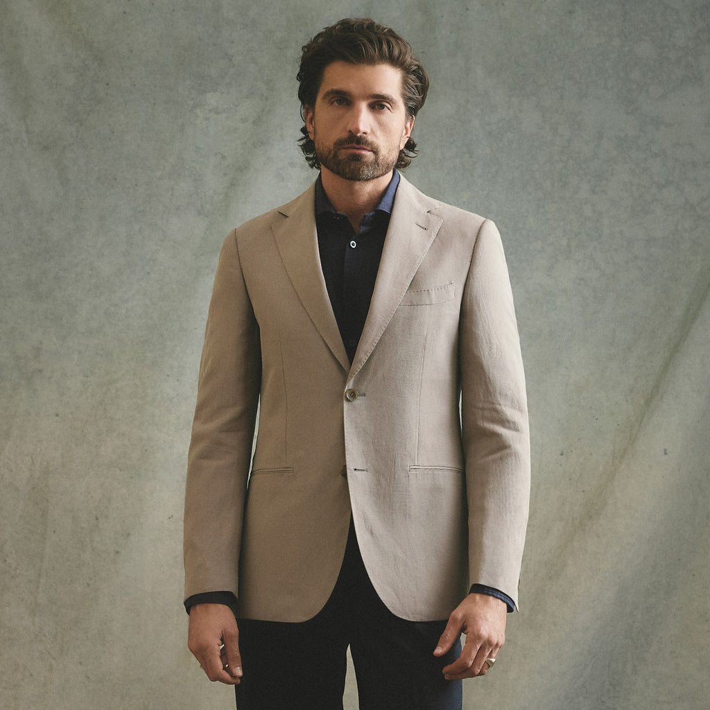 Man wearing a beige blazer over a dark shirt against a textured gray background