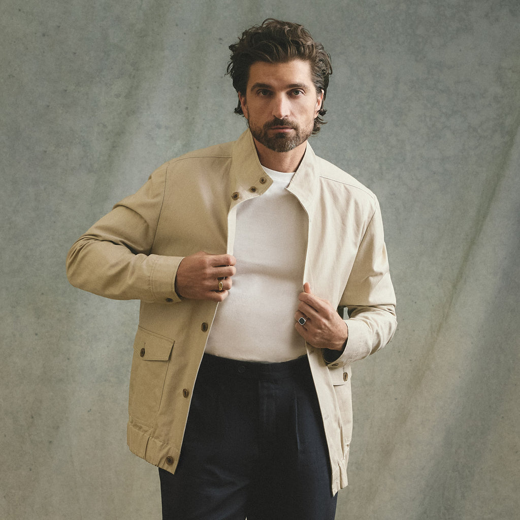 Man wearing a beige jacket over a white shirt against a textured gray background