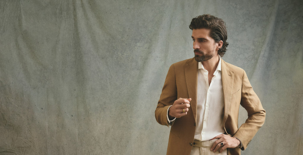 Man wearing a brown blazer over a white shirt against a textured gray background