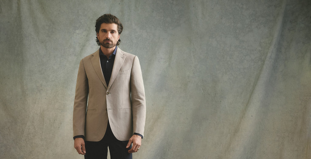 Man wearing a beige blazer over a black shirt against a textured gray background