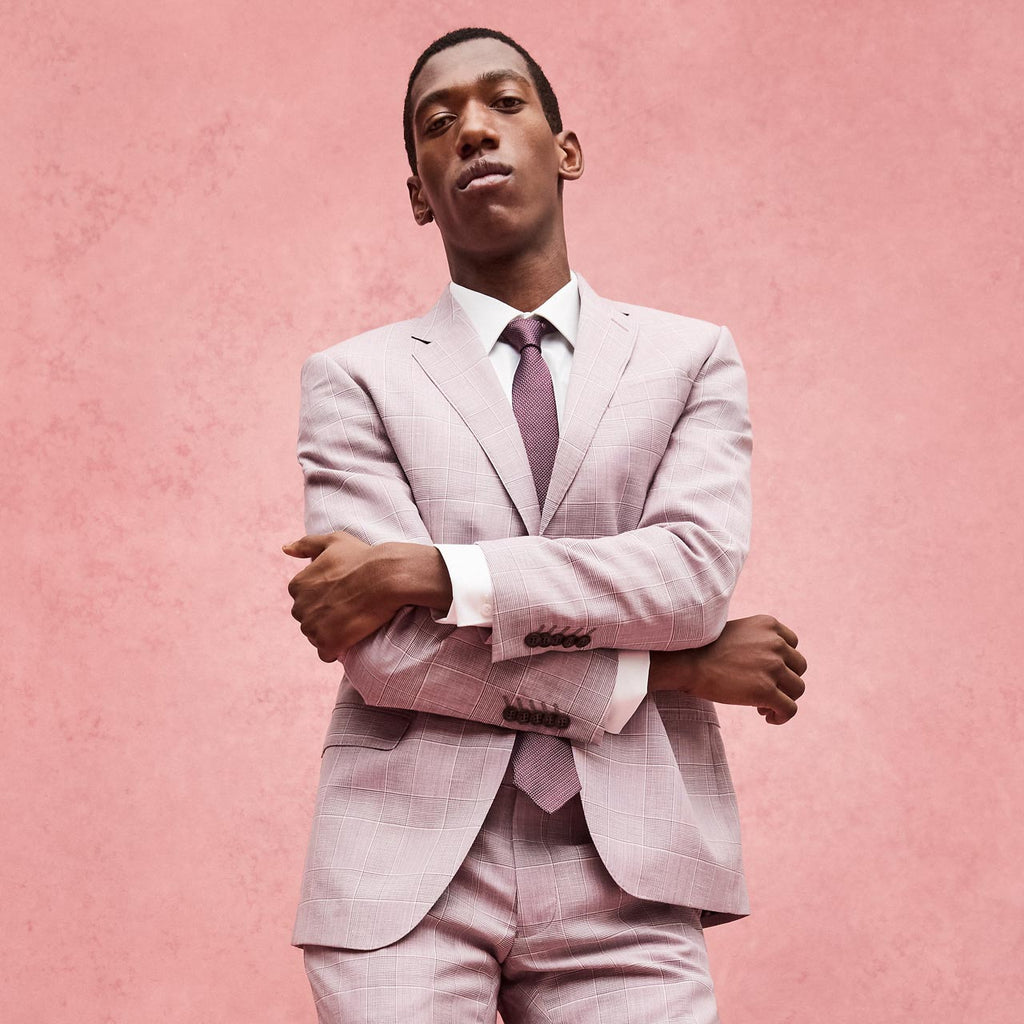 Man wearing a light pink suit with a purple tie against a pink background