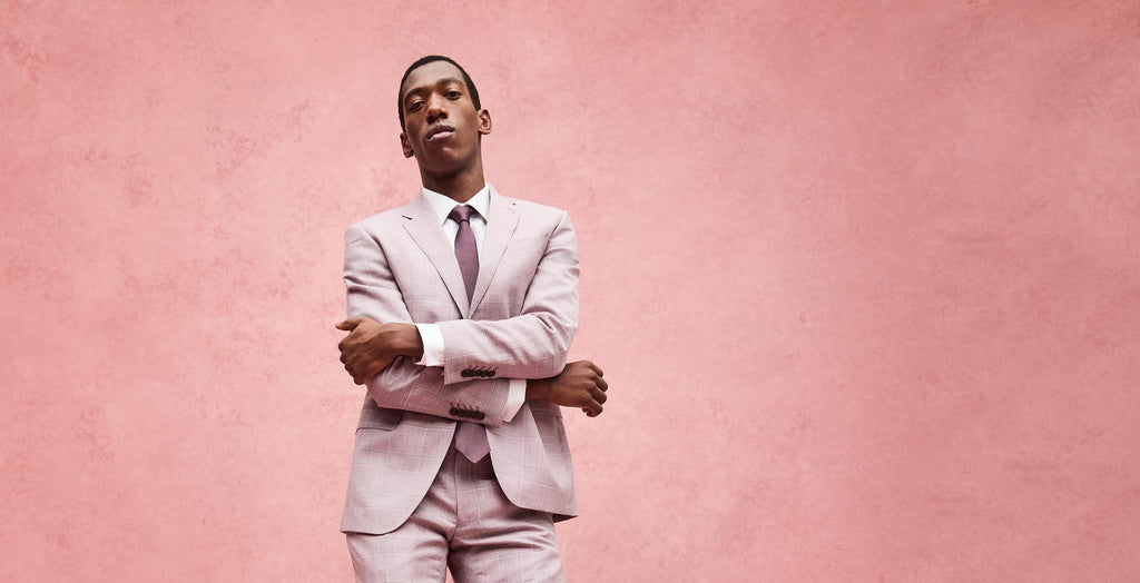 Man in a light gray suit standing against a pink background