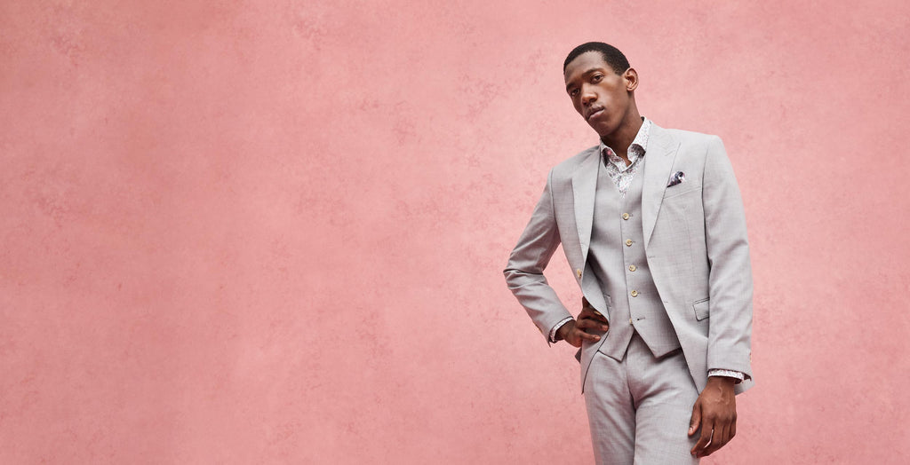 Man in a light gray suit standing against a pink background